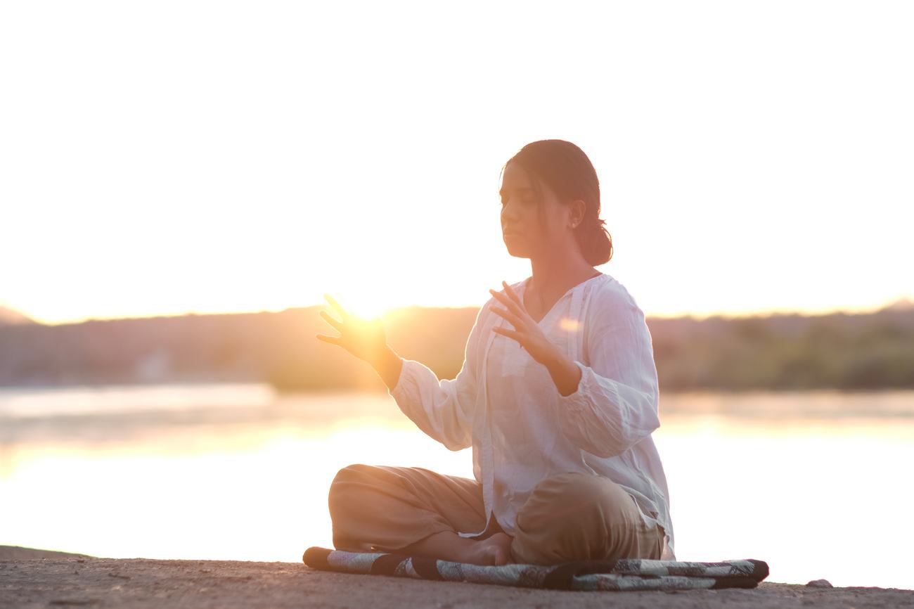 Woman meditating at sunset by a lake, hand raised